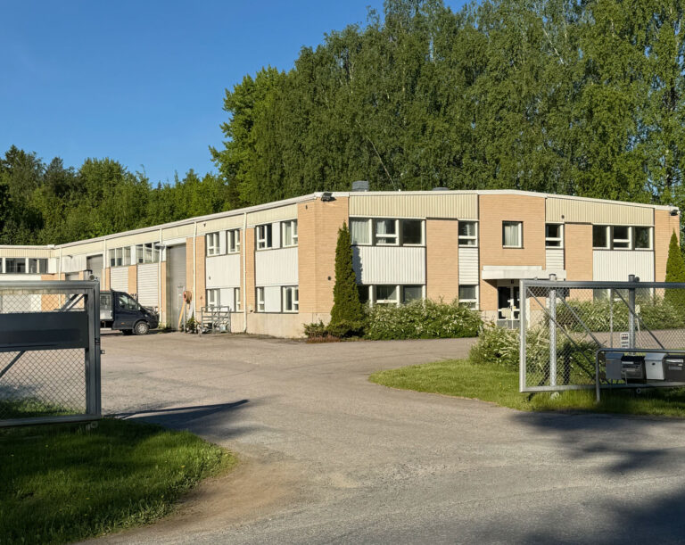 Vaalea toimisto- ja teollisuusrakennus sekä asfaltoitu piha-alue aidatulla tontilla.