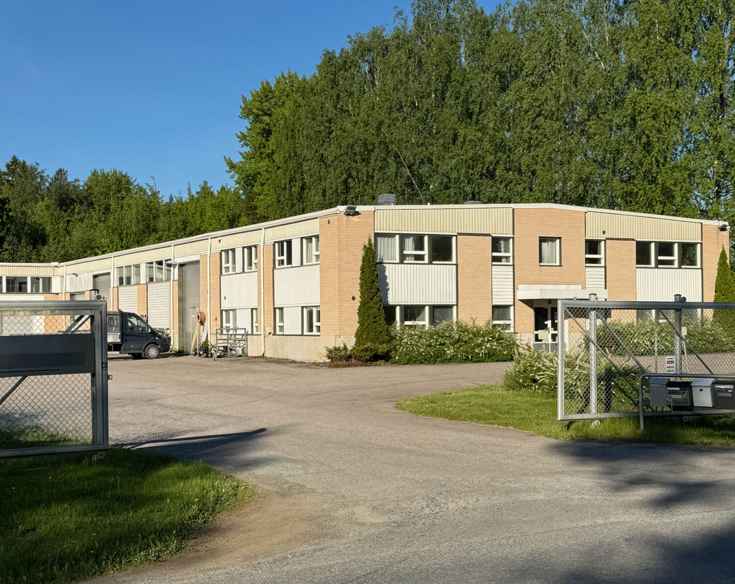 Vaalea toimisto- ja teollisuusrakennus sekä asfaltoitu piha-alue aidatulla tontilla.